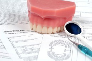 Dentures taking a bite out of a stack of dental bills and paperwork.